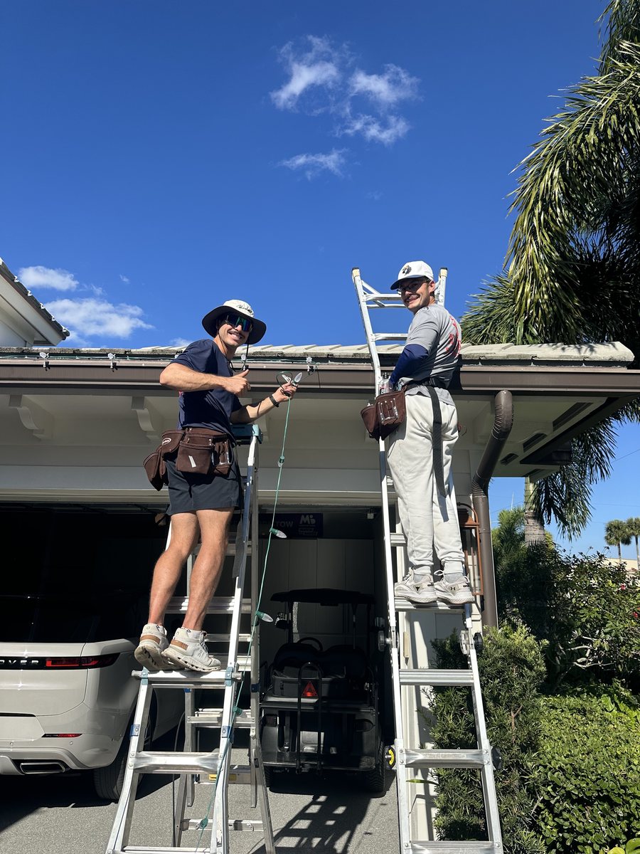 Stache Lights owner Kelsey Launi installing roofline lights on a ladder